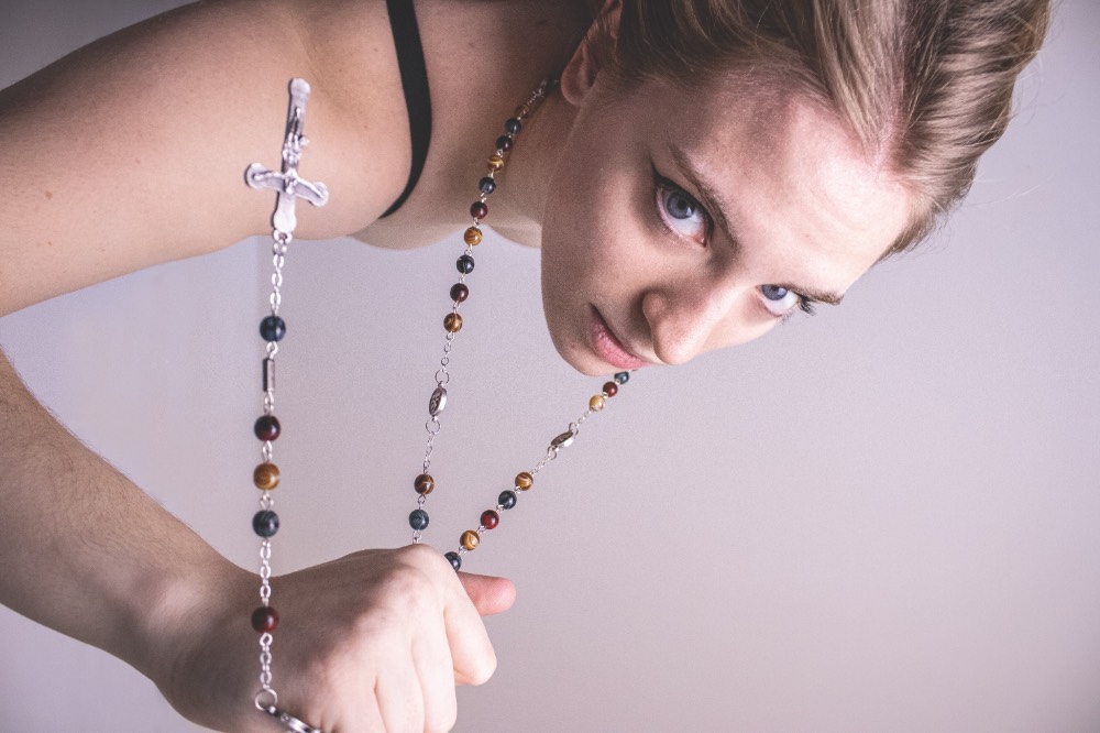 Color photo of a young woman clutching a rosary upside down.
